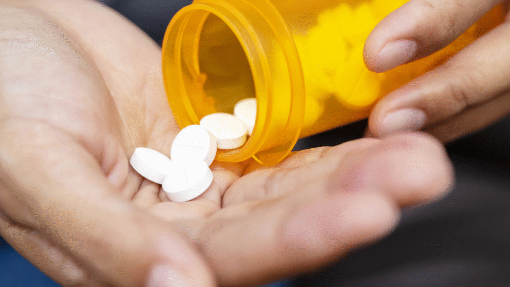 Hand pouring white prescription pills from an orange medicine bottle.