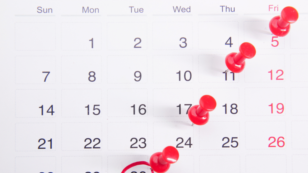 Close-up of a monthly calendar with multiple red push pins marking important clinical trial appointment dates.